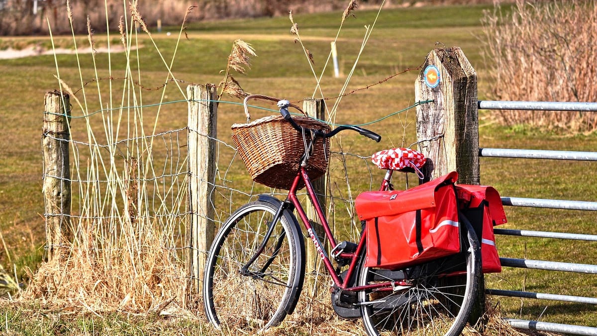 Vélo rouge équipé d'une double sacoche rouge sur le porte-bagage et d'un panier en osier, appuyé contre une clôture