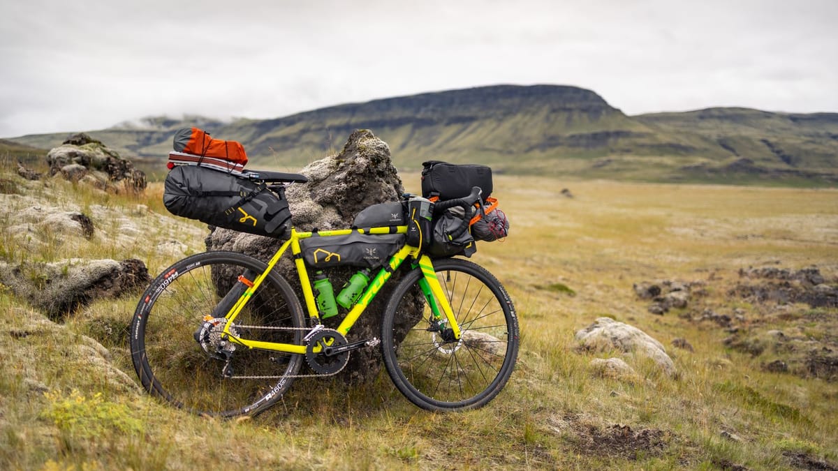 Vélo de bikepacking chargé de sacoches de selle, de cadre et de guidon, appuyé contre un rocher dans une lande