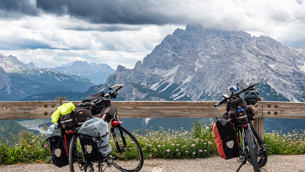 Deux vélos de voyage chargés de sacoches à fermeture enroulée, arrêtés devant un massif montagneux sous un ciel d'orage