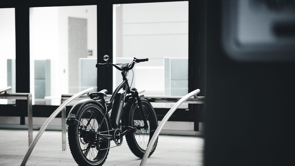 Vélo électrique à gros pneus garé entre deux arceaux, en noir et blanc