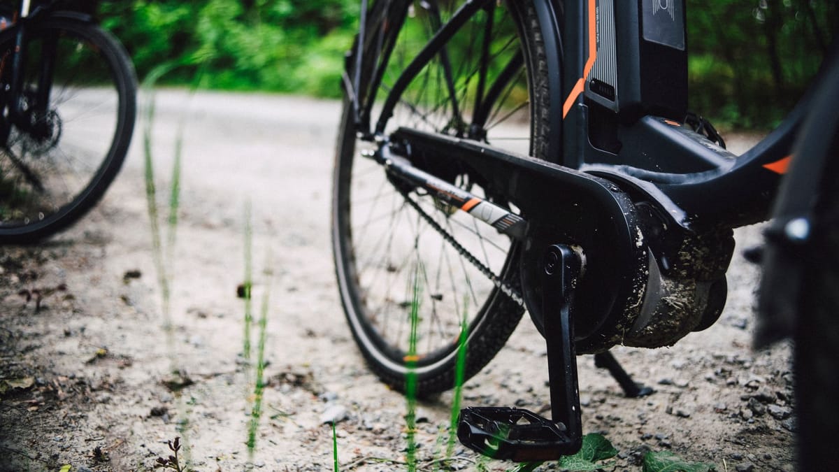 Gros plan sur le moteur central et la batterie d'un vélo électrique couvert de boue, arrêté sur un chemin